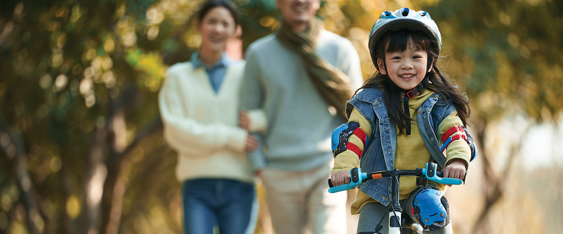 A girl riding a bike with her family walking in the background